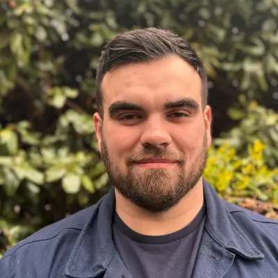 A man with a beard and mustache in front of bushes.