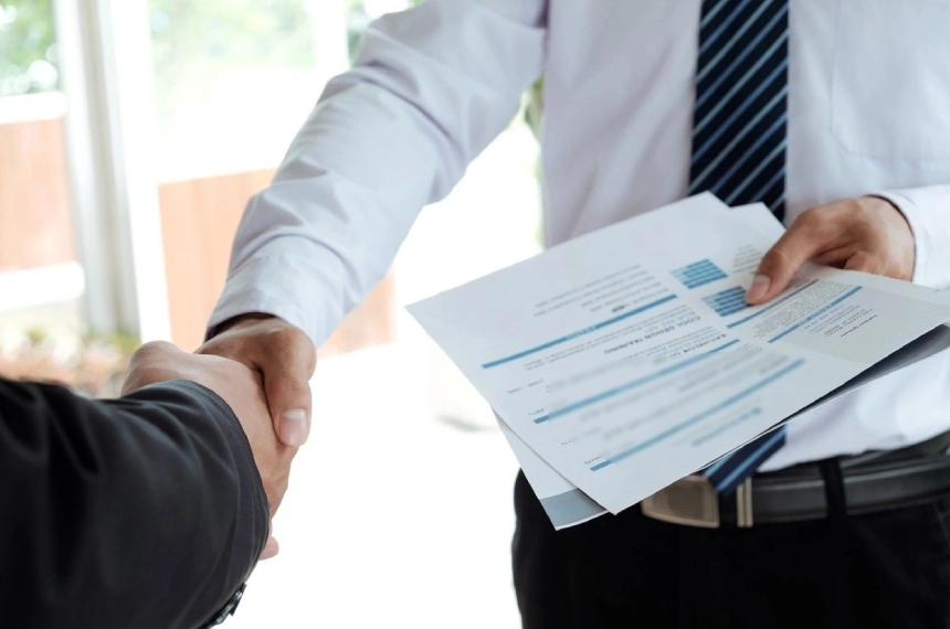 Two people shaking hands over a sheet of paper.