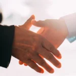 Two people shaking hands in front of a bright sky.