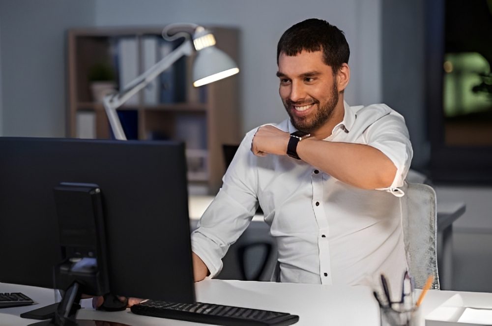Smiling man at desk checking smartwatch
