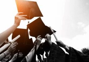 Graduate scheme celebration image with caps and diplomas raised outdoors in warm sunlight.